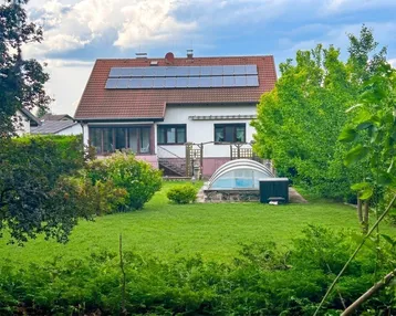 Großzügiger Gartenbereich mit Rasenfläche, Bäumen und einem überdachten Pool hinter dem Haus.