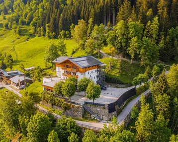 Luftaufnahme eines traditionellen Gebäudes mit Solarpaneelen auf dem Dach, umgeben von grünen Hügeln und Wäldern.