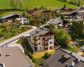 Luftaufnahme eines modernen Wohnhauses mit mehreren Balkonen in einer grünen Berglandschaft.