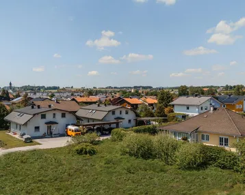 Blick über eine ländliche Wohnsiedlung mit Häusern und viel Grün unter blauem Himmel.