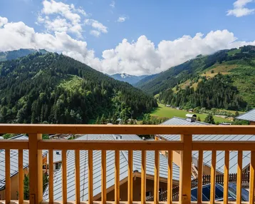 Panoramablick vom Balkon auf die majestätischen Berge und das grüne Tal unter blauem Himmel.