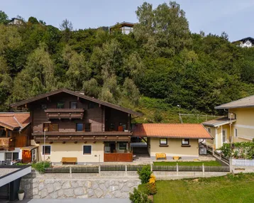 Traditionelles Haus mit Holzfassade und Ziegeldach, eingebettet in eine grüne Hanglandschaft.
