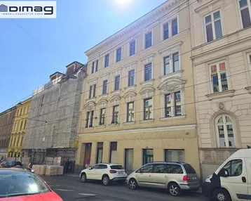 Historisches Gebäude mit gelber Fassade und vielen Fenstern an einer belebten Stadtstraße.