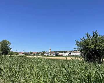 Weite ländliche Landschaft mit Feldern und einem Dorf mit Kirchturm in der Ferne.