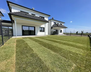 Frisch angelegter Rasen hinter modernen Reihenhäusern unter blauem Himmel.