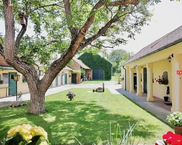 Grüner Innenhof mit großem Baum, gelben Gebäuden und gepflegtem Rasen, ideal zum Entspannen.