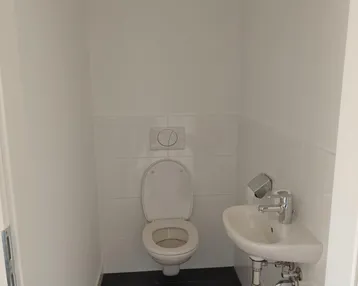 Kleines Gäste-WC mit wandhängender Toilette, Waschbecken und dunklen Bodenfliesen.