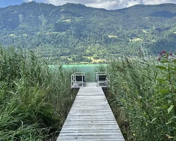 Ein Holzsteg führt durch hohes Schilf direkt zum See mit beeindruckendem Bergblick.