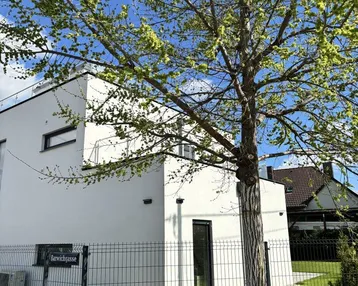 Modernes weißes Gebäude mit Flachdach, großen Fenstern und Klimaanlage im Außenbereich.