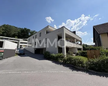 Moderne Wohnanlage mit mehreren Etagen, Balkonen und Zufahrt zur Tiefgarage, umgeben von viel Grün.