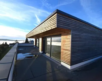 Große Dachterrasse mit moderner Holzfassade und weitem Blick über die neblige Landschaft.