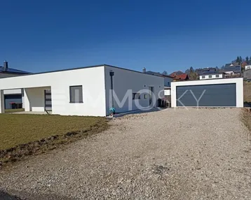 Moderne weiße Villa mit Flachdach, Kiesauffahrt und separater Garage unter blauem Himmel.