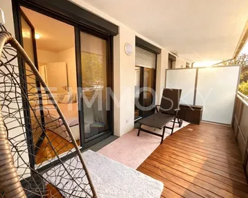 Sonniger Balkon mit Holzfußboden, Hängesessel und Blick in den Innenbereich.