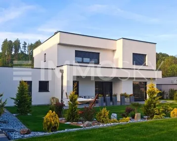 Modernes Einfamilienhaus mit gepflegtem Garten und Terrasse, umgeben von grüner Landschaft.