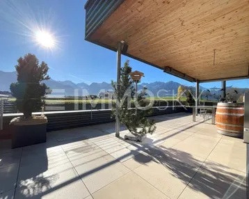 Sonnige Terrasse mit Holzdach, Fliesenboden und beeindruckendem Bergblick.