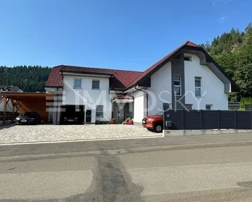 Modernes Einfamilienhaus mit Satteldach, Carport und gepflasterter Einfahrt unter blauem Himmel.