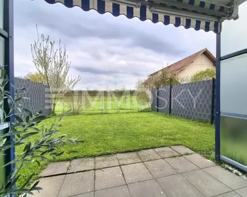 Gepflasterte Terrasse mit Markise und Blick auf den privaten Gartenbereich mit Rasenfläche.