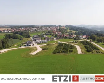 Luftaufnahme einer ländlichen Gegend mit einem Dorf im Hintergrund und grünen Feldern.