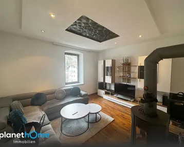 Gemütliches Wohnzimmer mit Holzboden, modernem Kaminofen und Blick ins Grüne.