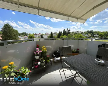 Möblierter Balkon mit Markise, Pflanzen und weitem Blick über die Wohnsiedlung und grüne Umgebung.