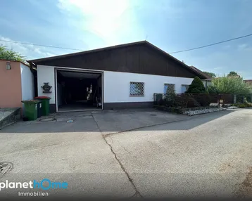 Geräumige Garage mit offenem Tor und gepflasterter Zufahrt, umgeben von kleinen Grünflächen.