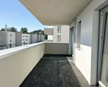 Langer, schmaler Balkon im Rohbauzustand mit Blick auf weitere Neubauten und sonnigen Himmel.