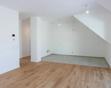 Helles, unmöbliertes Zimmer mit Holzboden und Fliesenbereich, ideal für Wohnen und Küche.