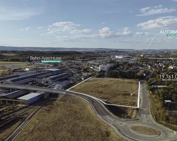 Luftaufnahme eines großen Grundstücks in einem Industriegebiet mit Autobahn- und Bahnanschluss in der Ferne.