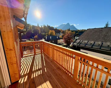 Sonnige Holzterrasse mit Bergblick und traditionellem Geländer, ideal zum Entspannen im Freien.