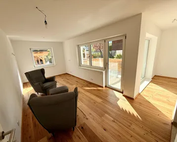 Helles Wohnzimmer mit Holzboden, großen Fenstern und Zugang zu einem Außenbereich.