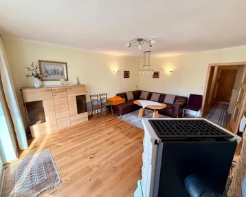 Gemütliches Wohnzimmer mit Holzboden, Ecksofa und einem modernen Kaminofen für behagliche Wärme.