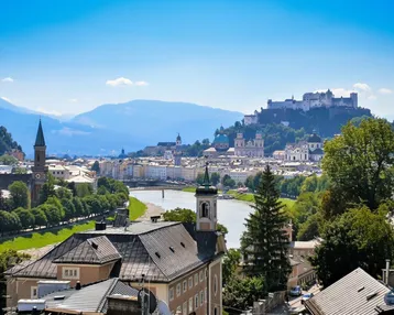 Panoramablick über die historische Stadt Salzburg mit Fluss, Gebäuden und majestätischen Bergen im Hintergrund.