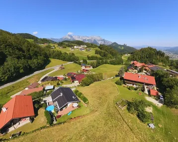 Panoramablick aus der Vogelperspektive auf eine ländliche Siedlung mit grünen Hügeln und majestätischen Bergen im Hintergrund.