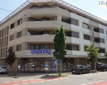 Modernes Mehrfamilienhaus mit Geschäften im Erdgeschoss und Balkonen in urbaner Umgebung.
