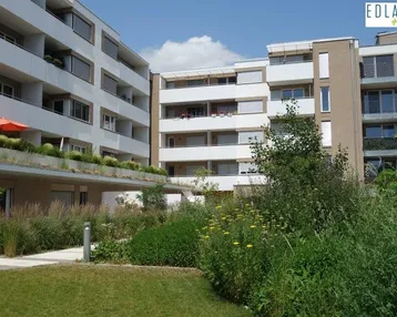 Moderne Wohngebäude mit begrüntem Innenhof, Balkonen und gepflegten Grünflächen.