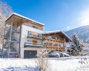 Modernes Gebäude mit Balkonen und Außentreppe, umgeben von verschneiter Winterlandschaft und Bergen.