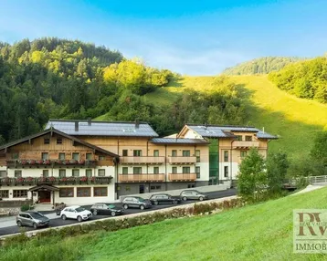 Großes Gebäude im alpinen Stil, umgeben von grünen Hügeln und Wäldern.