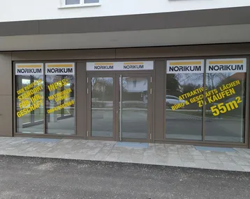 Moderne Geschäftsfassade mit großen Schaufenstern und Werbeaufklebern für eine Gewerbefläche.