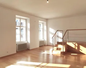 Helles Wohnzimmer mit Holzparkettboden, großen Fenstern und einer Treppe zu einem erhöhten Bereich.