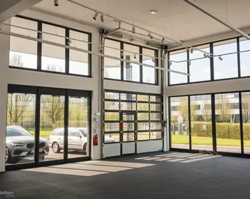 Großer, heller Gewerberaum mit hohen Decken, großen Fensterfronten und einem Rolltor, ideal als Showroom.