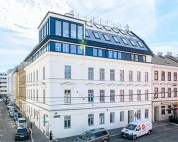 Modernisiertes Mehrfamilienhaus mit neuem Dachausbau und klassischer Fassade an einer Stadtstraße.