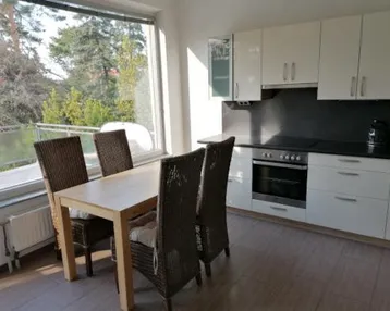 Moderne Küche mit weißen Schränken, Essbereich und großem Fenster mit Blick ins Grüne.