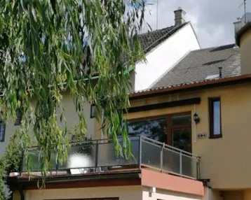 Gebäudeansicht mit einem Balkon, der von einem Baum teilweise verdeckt wird und eine grüne Aussicht bietet.