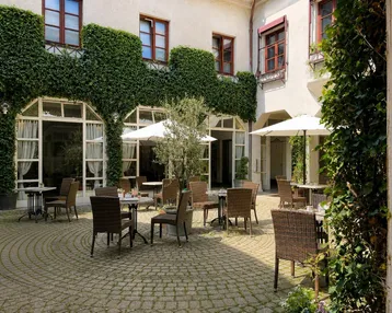 Gemütlicher Innenhof mit Tischen, Stühlen und Sonnenschirmen, umgeben von einer mit Efeu bewachsenen Fassade.