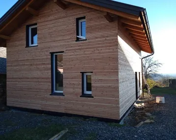 Neubau eines Einfamilienhauses mit Holzfassade und Satteldach in ländlicher Umgebung.