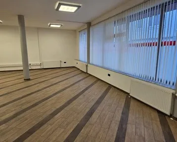Geräumiger, leerer Büroraum mit großen Fenstern, Jalousien und Holzboden in gutem Zustand.