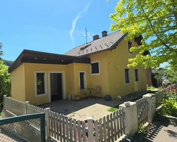 Gelbes Einfamilienhaus mit Satteldach, kleinem Vorgartenbereich und sonnigem Wetter.