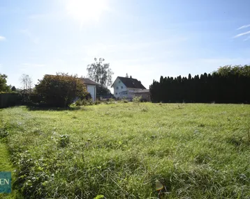 Weitläufiges Grundstück mit grüner Wiese und umliegenden Wohnhäusern unter blauem Himmel.