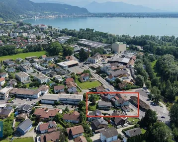 Luftaufnahme einer Stadt am See mit Bergen im Hintergrund, das Grundstück ist rot markiert.