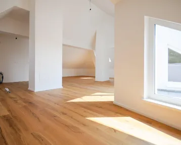 Heller, offener Raum im Dachgeschoss mit Holzboden und großen Fenstern, bereit für die Einrichtung.